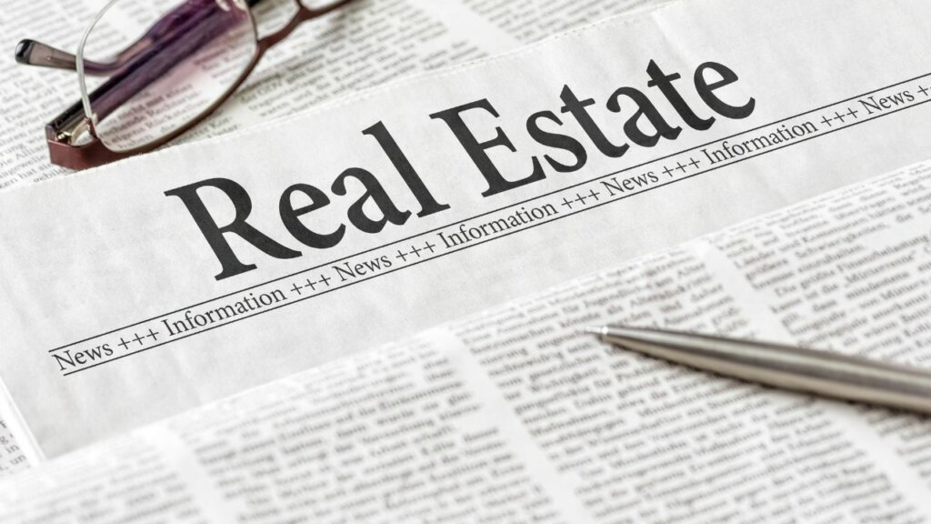 News Paper with words Real Estate as heading, a pen and glasses sitting on the paper.