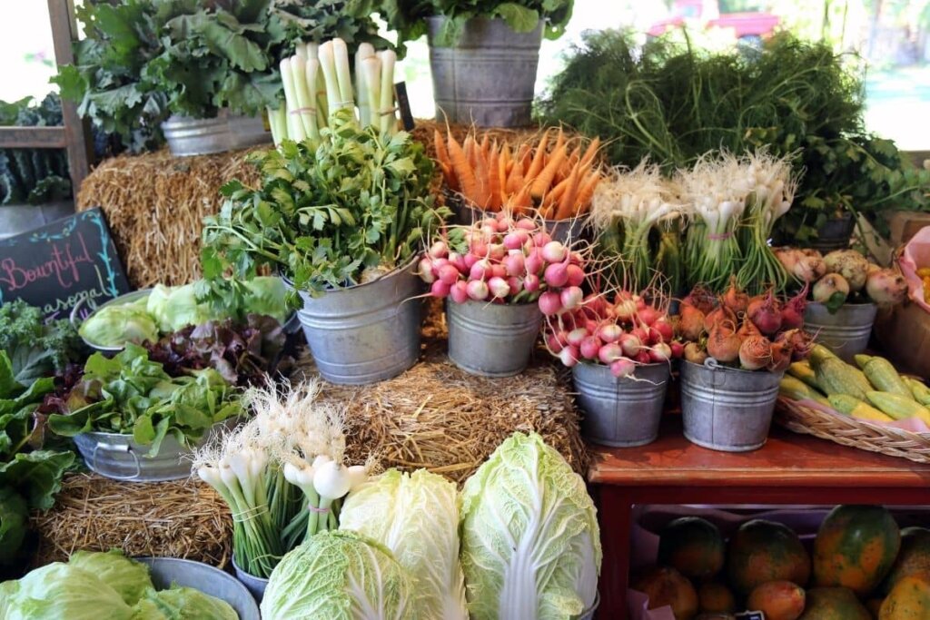Fresh vegetables being displayed on a wood table and bails of hay at a farmer's market.