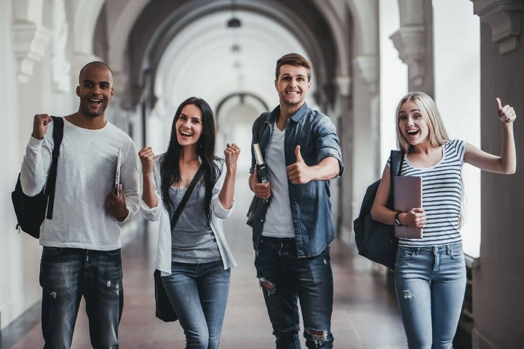 Four happy students walking down a long university hallway.