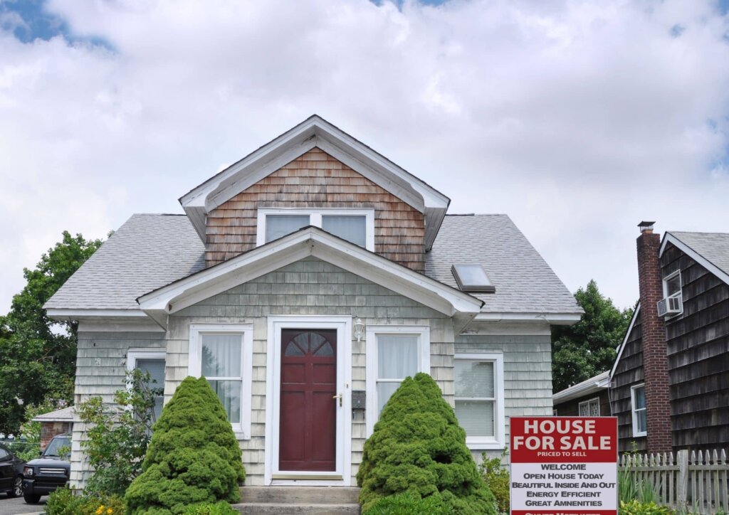 quaint home with red door and for sale sign in yard