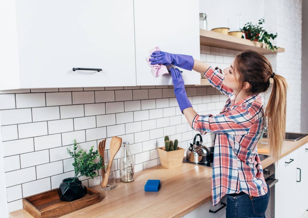a woman cleaning kitchen cabinets with purple gloves on