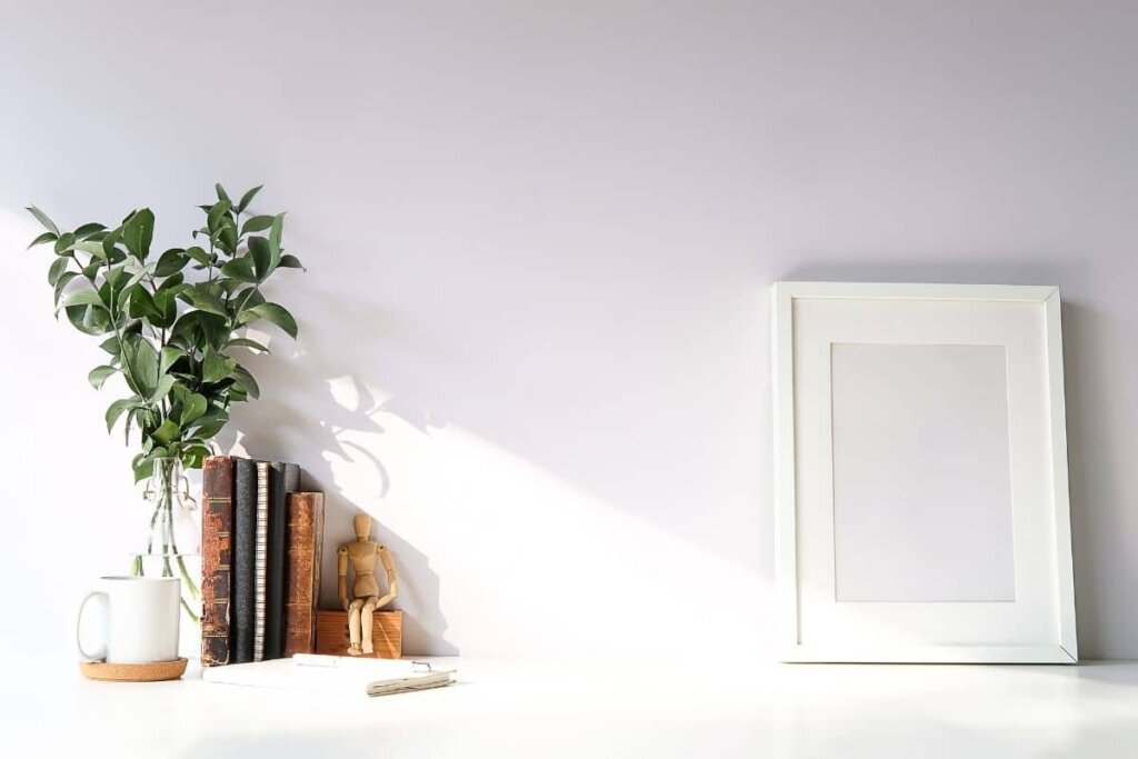white shelf with a vase of green leaves and old books, a frame with no picture in it