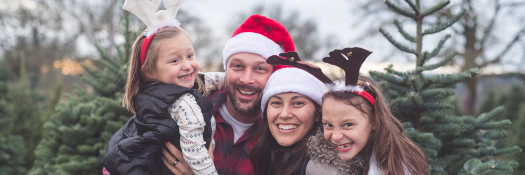 Family posing in front of Christmas tree farm