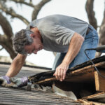 Close up view of man removing rotten wood from leaky roof