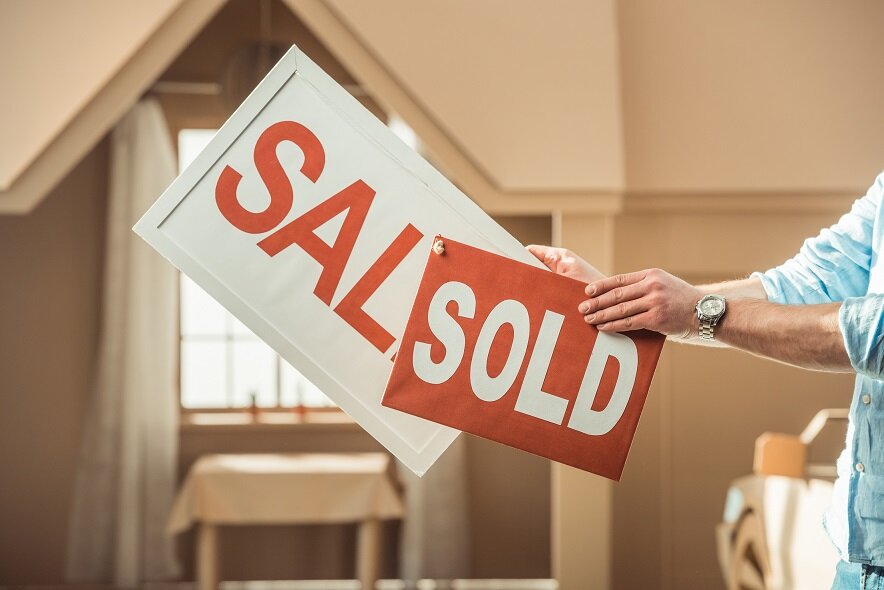 cropped shot of man holding sale and sold signboards in front of cardboard house