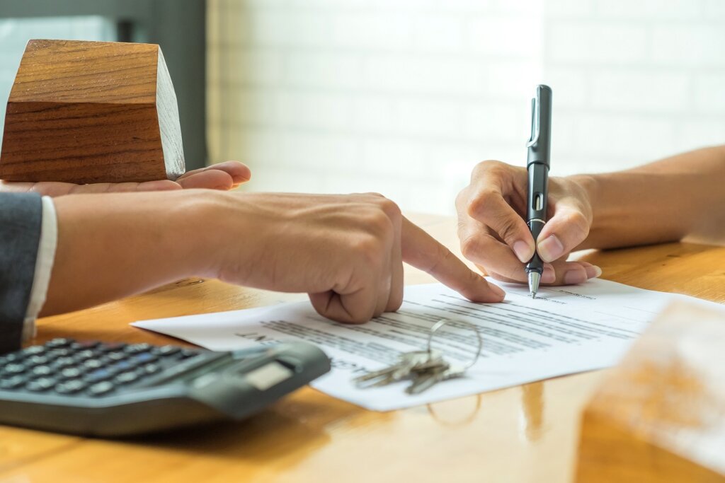 Buyers are signing a home purchase agreement from a broker,model house in broker hand and calculator with a house key on the table.