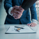 two people shaking hands over a contract for a house with the keys on top of the contract