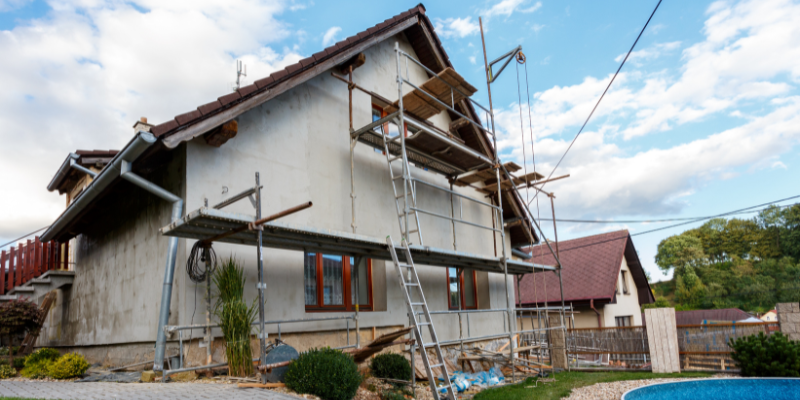 a house with scaffolding everywhere and two ladders, with the garden torn up