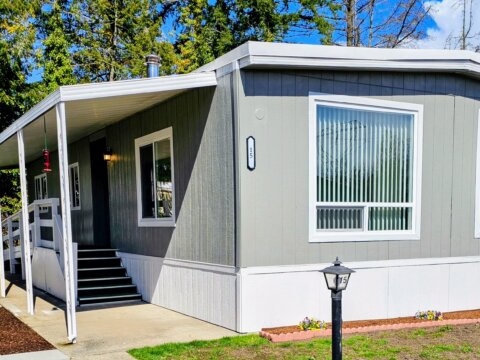 Beautiful double-wide manufactured home with two large windows and deck covered with an awning.