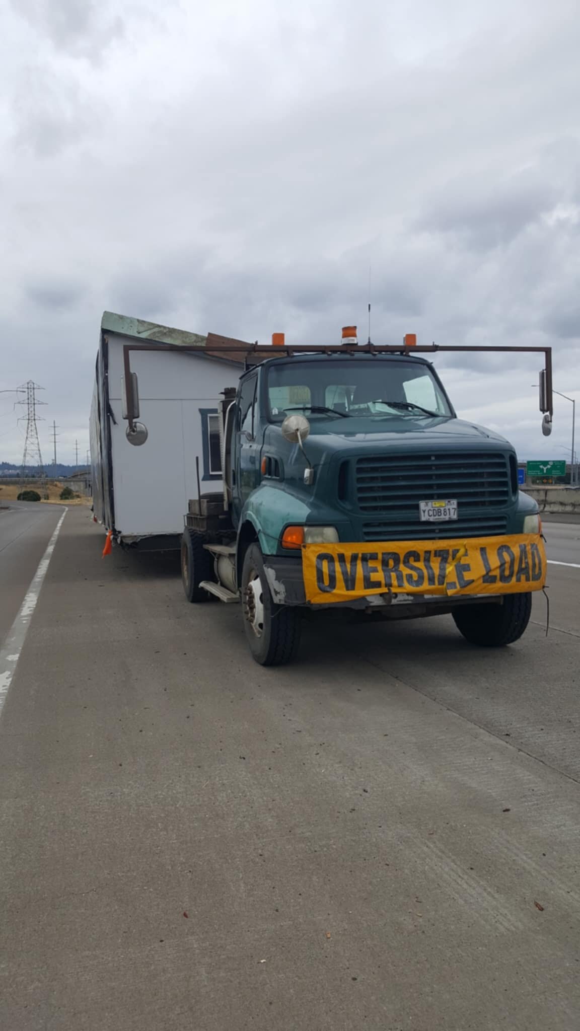 A semi truck with extended mirrors and an "Oversized Load" sign on the front towing a manufactured home behind it. 