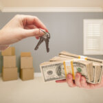 Man and Woman Handing Over Cash For House Keys Inside Empty Gray Room with Boxes.