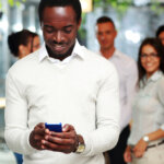 Happy businessman using smartphone in front of colleagues