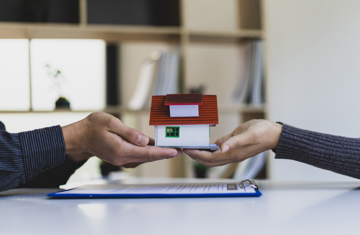 Stock photo for inherited house: two pairs of hands holding a small model house over title transfer paperwork.