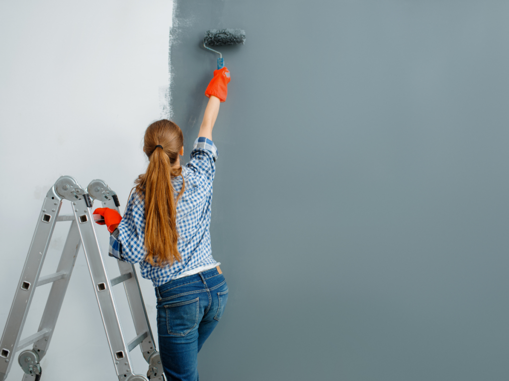 A woman on a ladder painting a wall with a roller