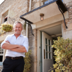 A landlord standing in front of the open door of a stone-faced rental property