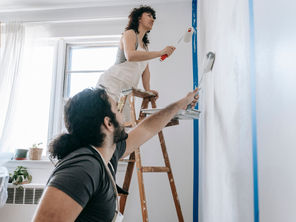 A man and a woman painting a white wall with rollers.