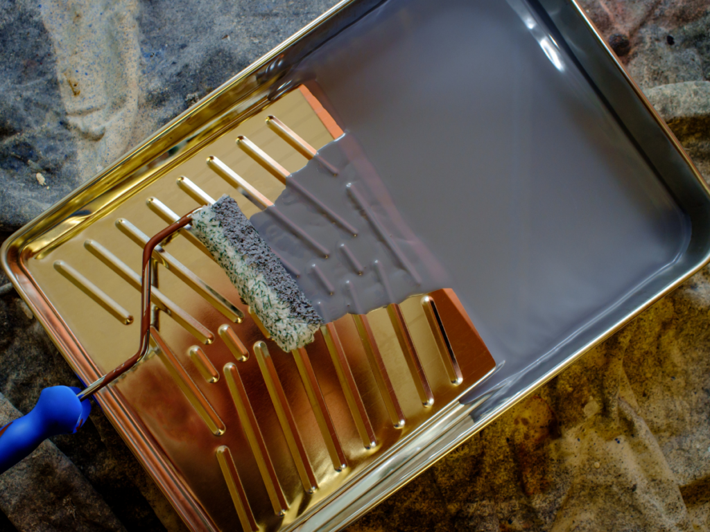 A bronze paint tray filled with gray paint and a small roller.