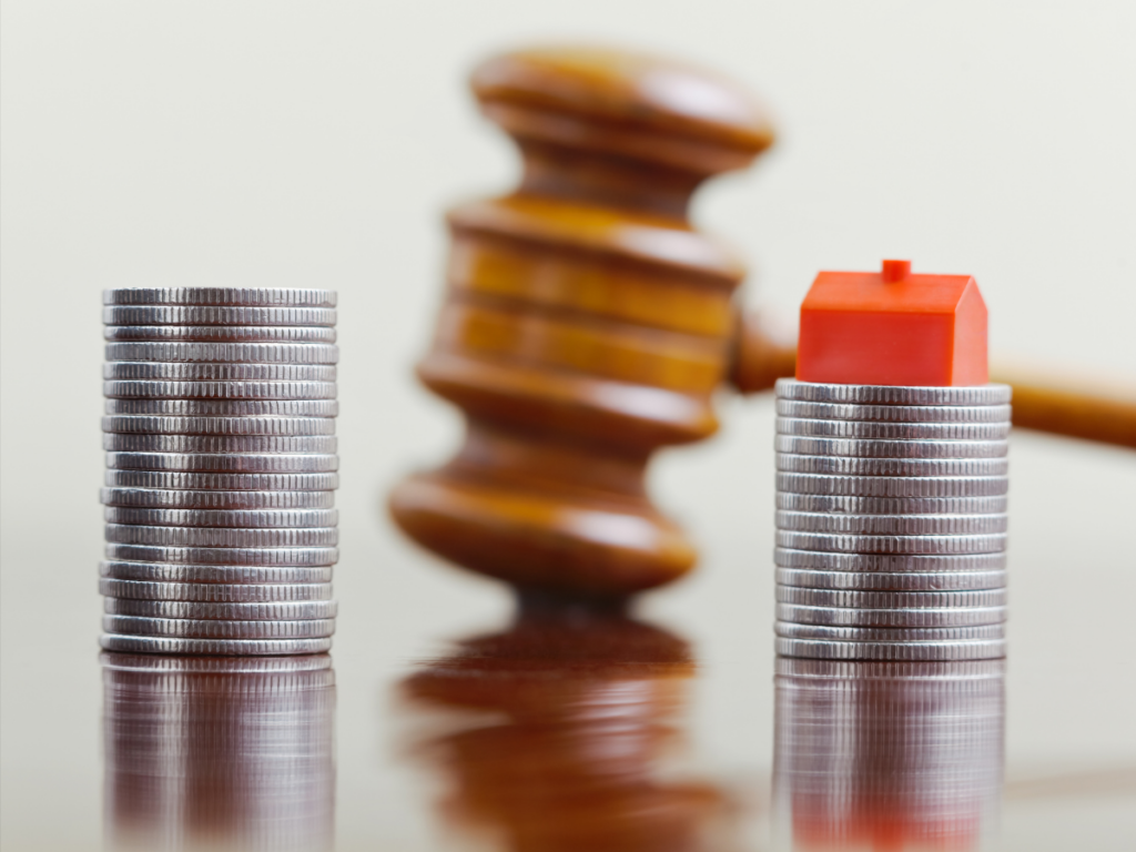 A stock image for dividing assets: two stacks of coins, one with a house figuring on top. In the background is a gavel.