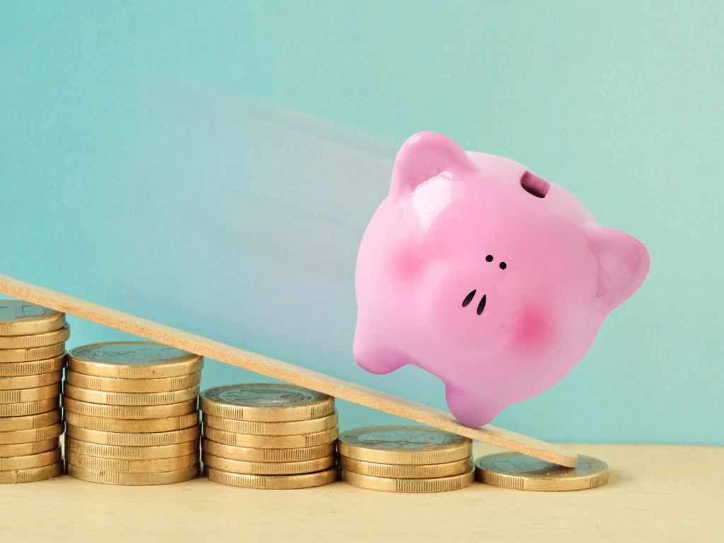 Stock image for losing money: a piggy bank falling down piles of coins.
