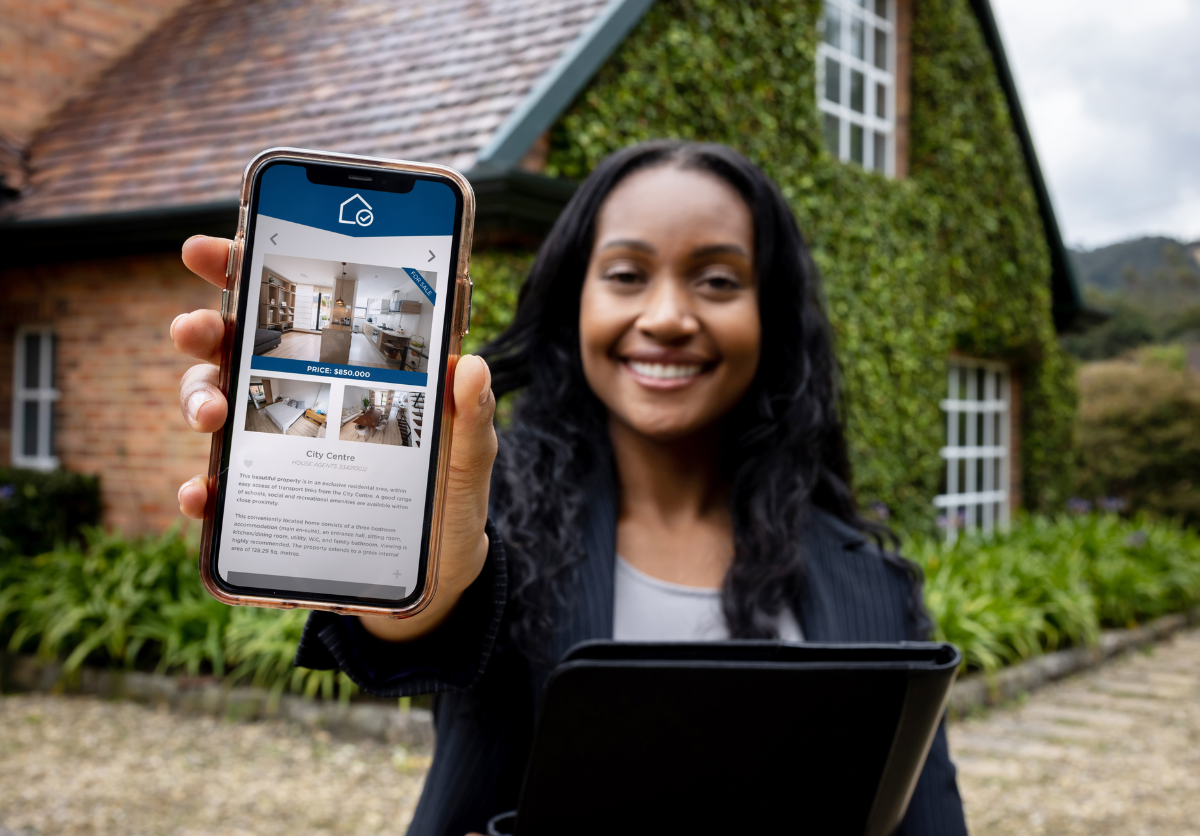 A real estate agent standing in front of a house, holding a clipboard and a phone with a listing pulled up.
