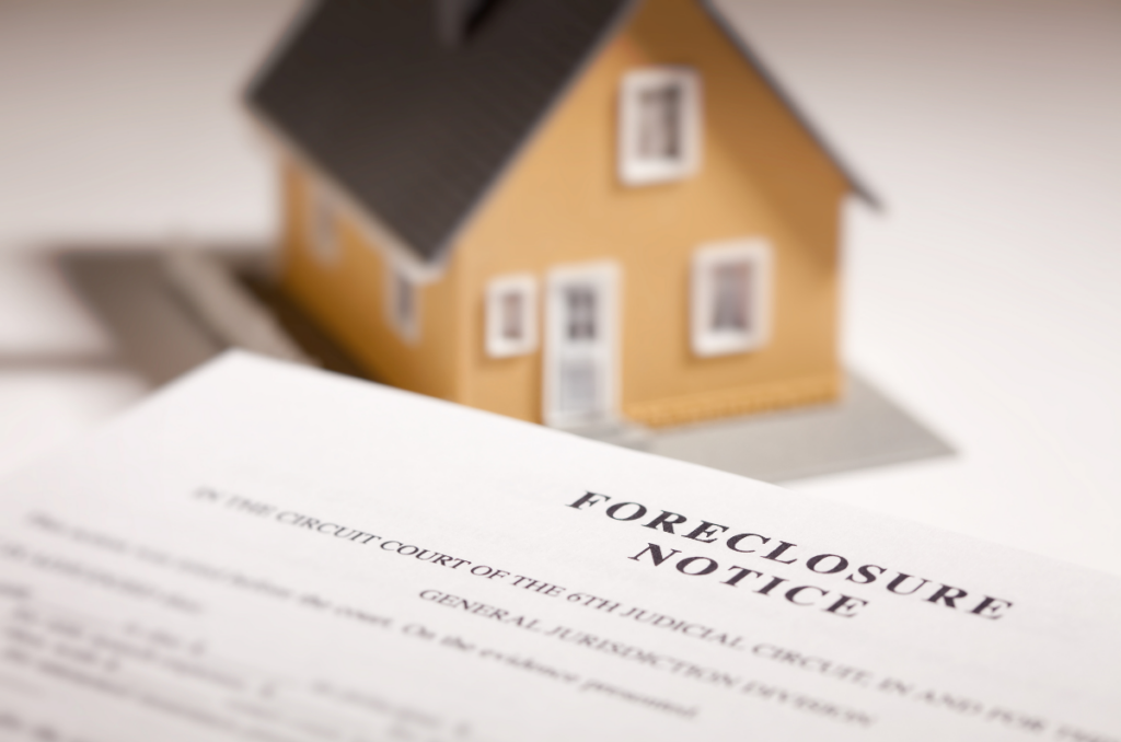 A foreclosure notice in front of a yellow miniature house