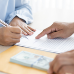Hands signing a contract beside a stack of money