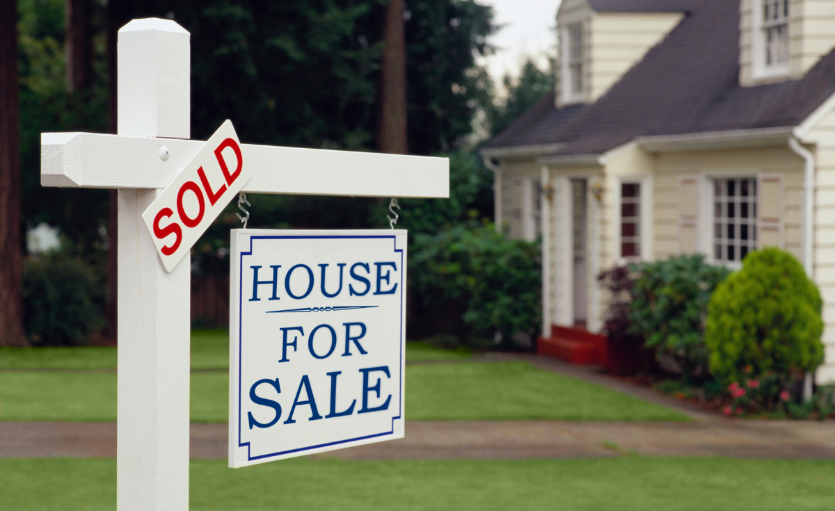 A "Sold" and "House for Sale" sign in the front yard of a home