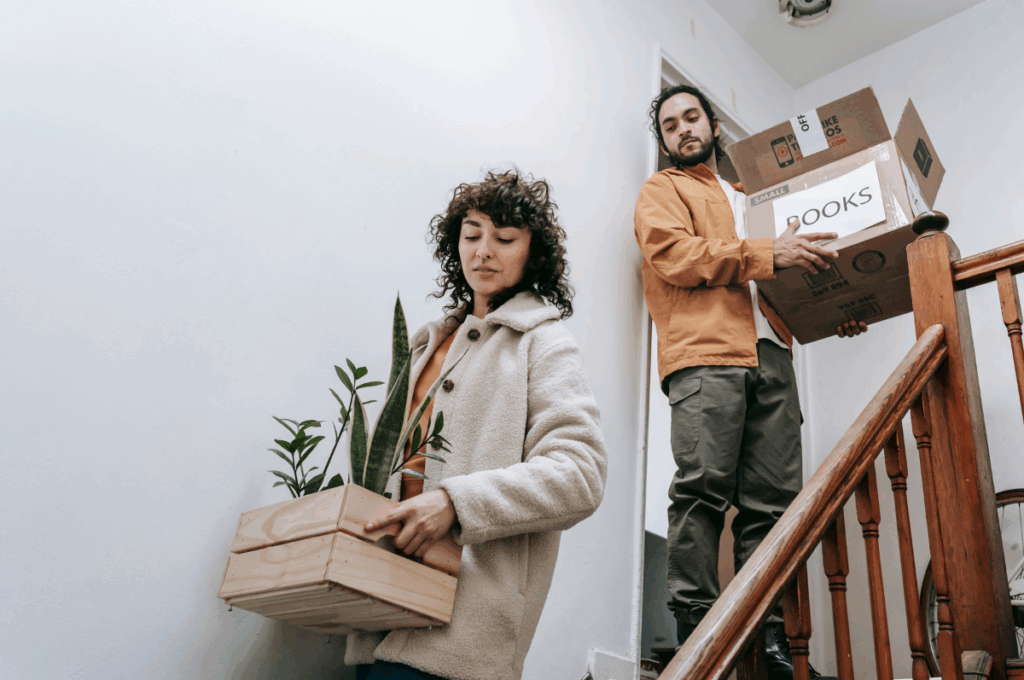 A man and a woman moving packed boxes down a flight of stairs.