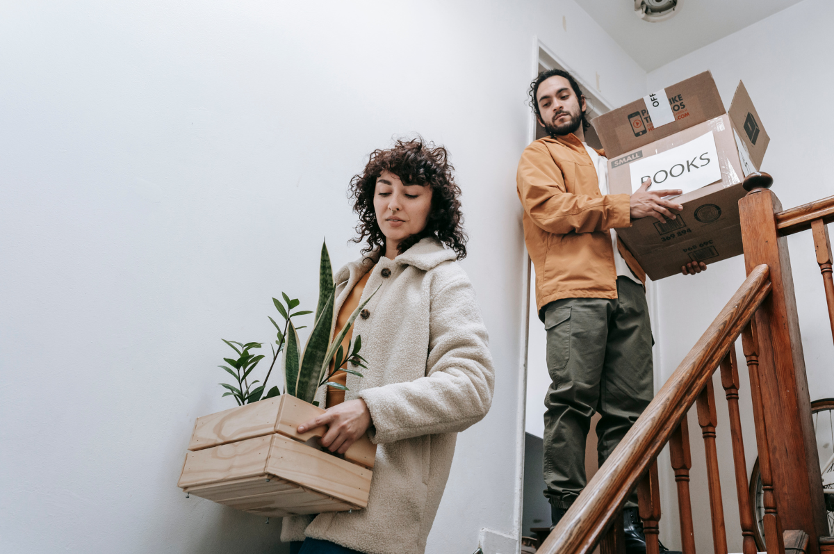 A man and a woman moving packed boxes down a flight of stairs.