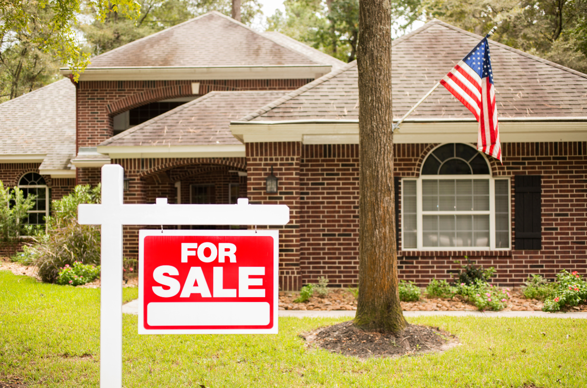 A house with a "For Sale" sign in the front yard