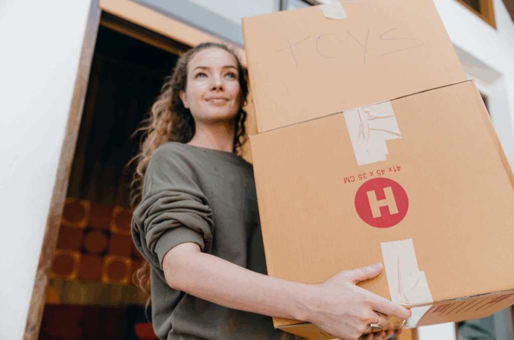 A woman carrying a stack of boxes out of a house.