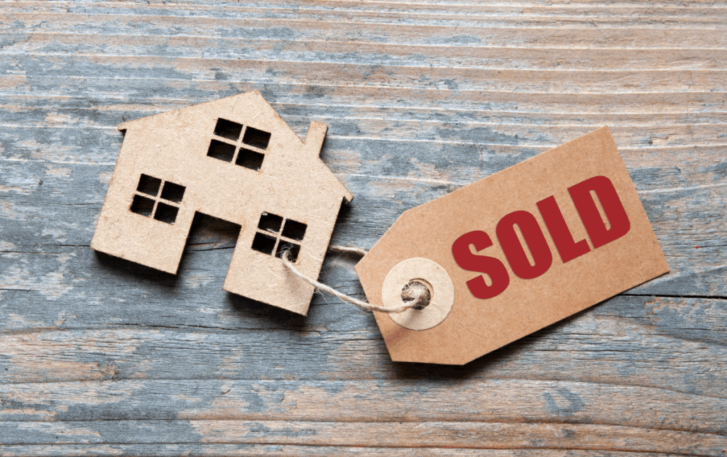 A cardboard house cutout with a "Sold" tag.