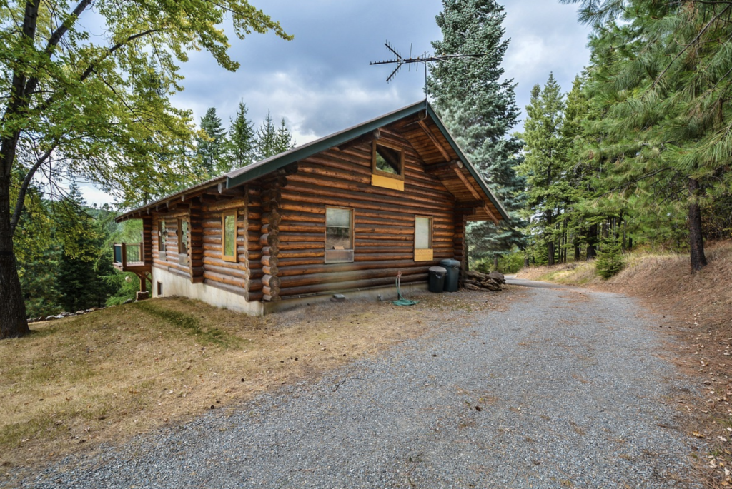 A log cabin along a gravel road surrounded by evergreen trees