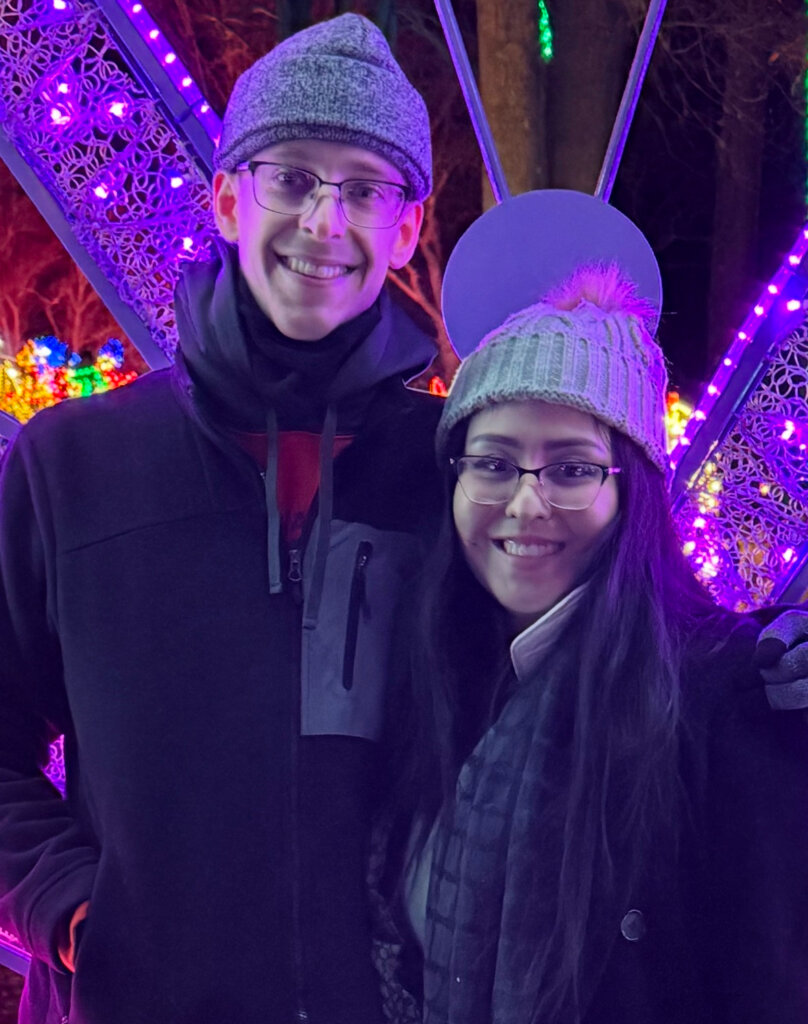 Jacob and Jackie smiling together in front of a colorful holiday-lights display