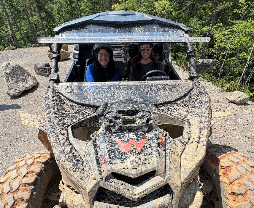 Jackie and Jacob smiling from the seats of a mud-covered side-by-side UTV on a wooded trail in Gatlinburg