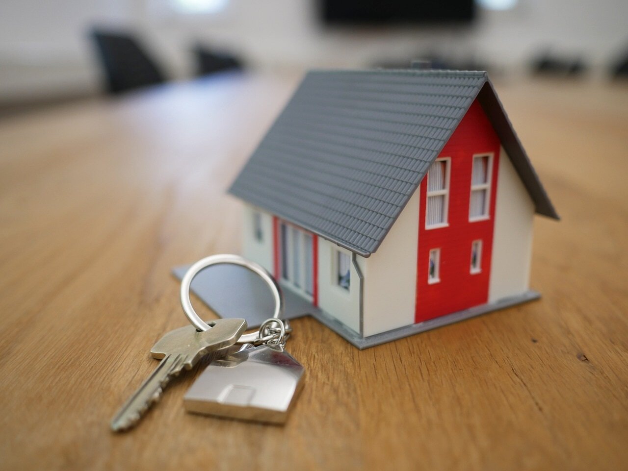 A miniature house and key on a wooden desk.