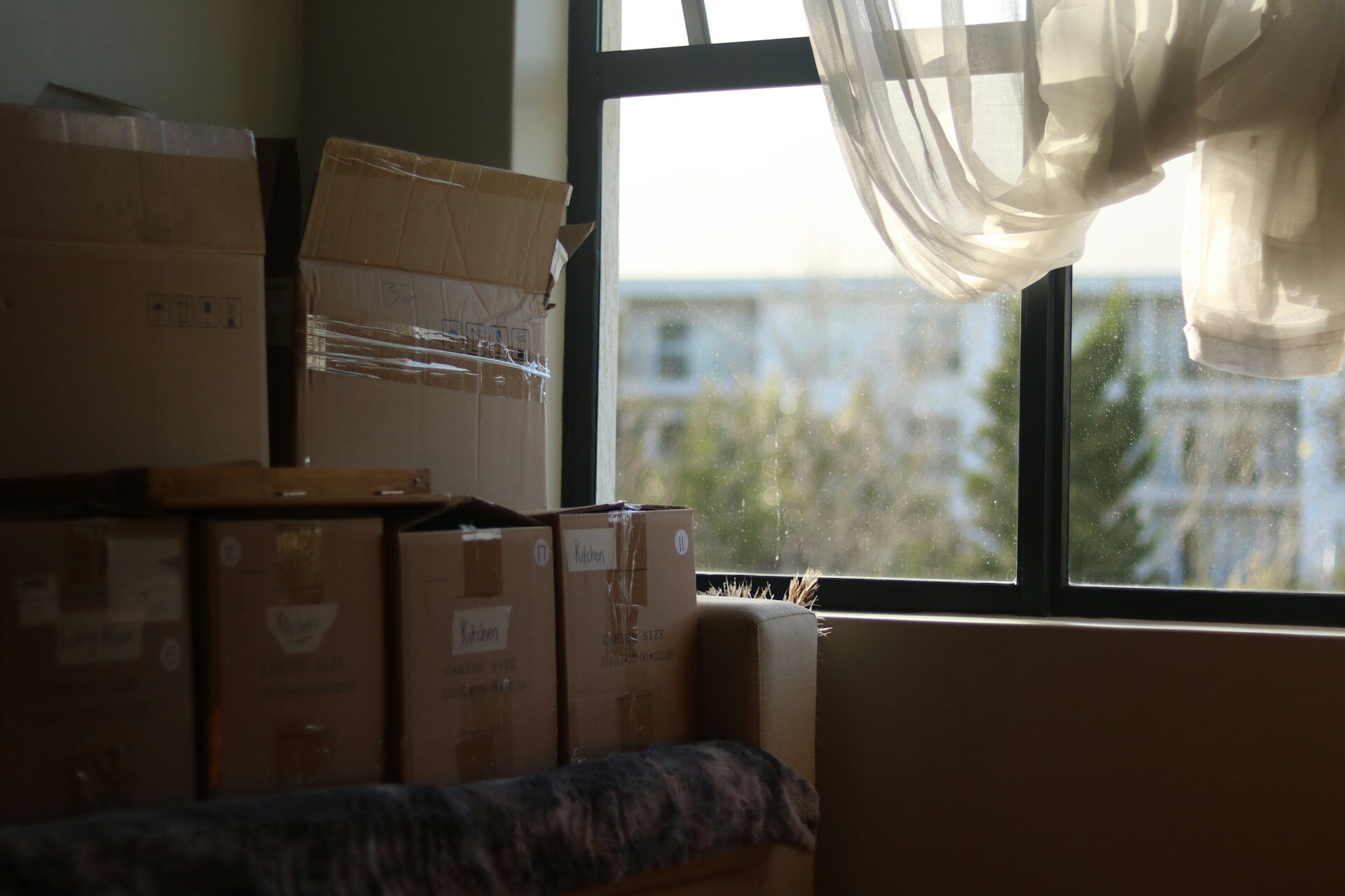 Cardboard boxes for moving, stacked one on top of the other near the window.