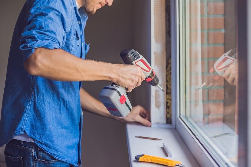A man with a drill and an exacto knife fixing a window.