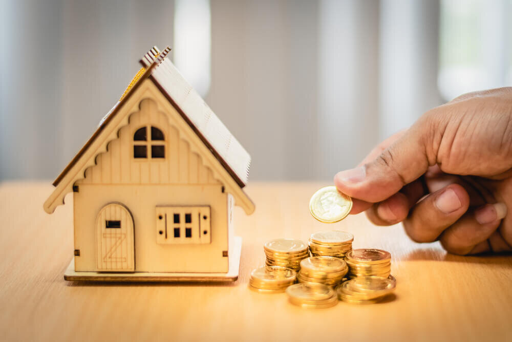 Hand holding coins next to a miniaturized house