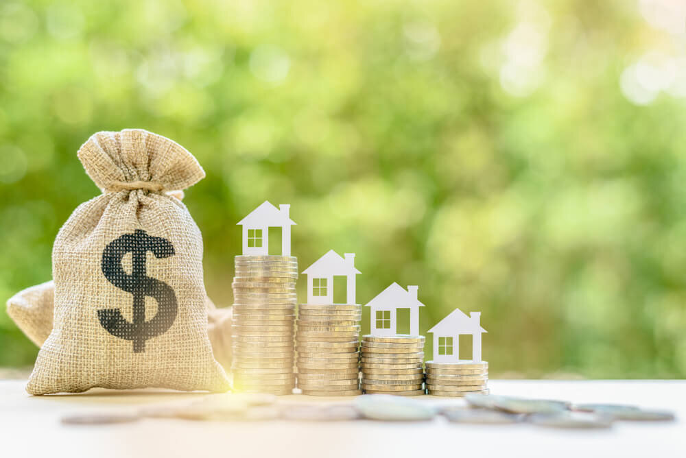 bag of cash next to piles of coins with miniature houses on top of each