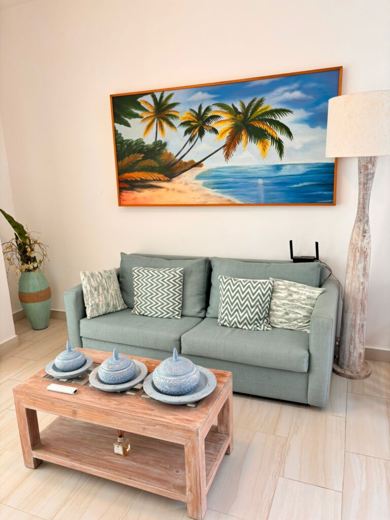 Modern Punta Cana vacation condo living room with sofa, tropical wall art, and natural light.
