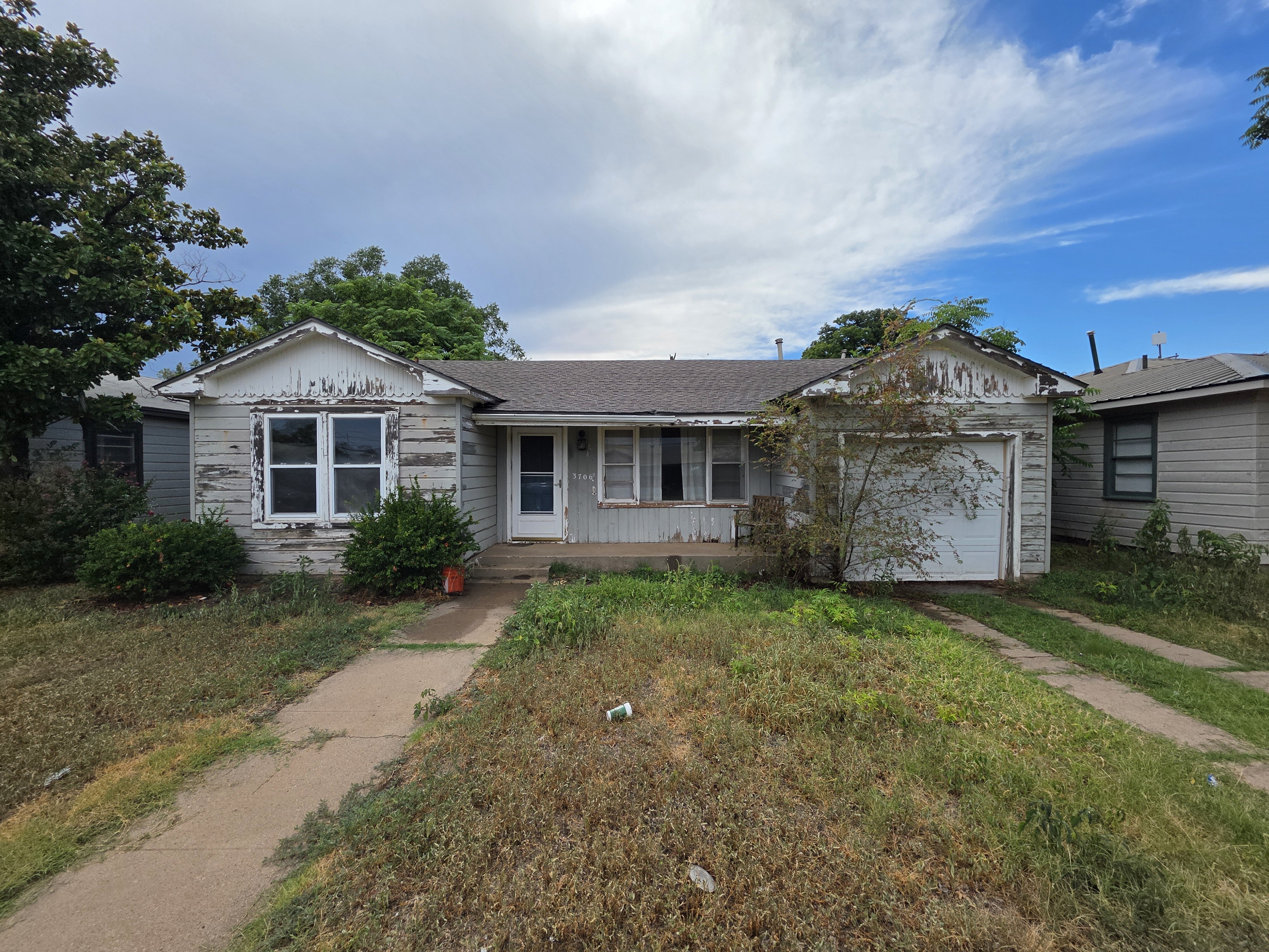 Run-Down Single-Story House In Lubbock Texas With Peeling Paint, Overgrown Yard, And Outdated Exterior, Showing That Cash Home Buyers Like Electrum Purchase Properties As-is And Help Homeowners Sell Your House Fast For Cash