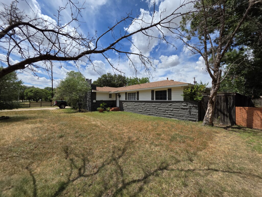 Single-Story Ranch House In Lubbock Texas With Large Front Yard, Stone Siding, And Surrounding Trees, Showing That Cash Home Buyers Purchase Properties Of Any Size Or Condition And Help Homeowners Sell Your House Fast For Cash