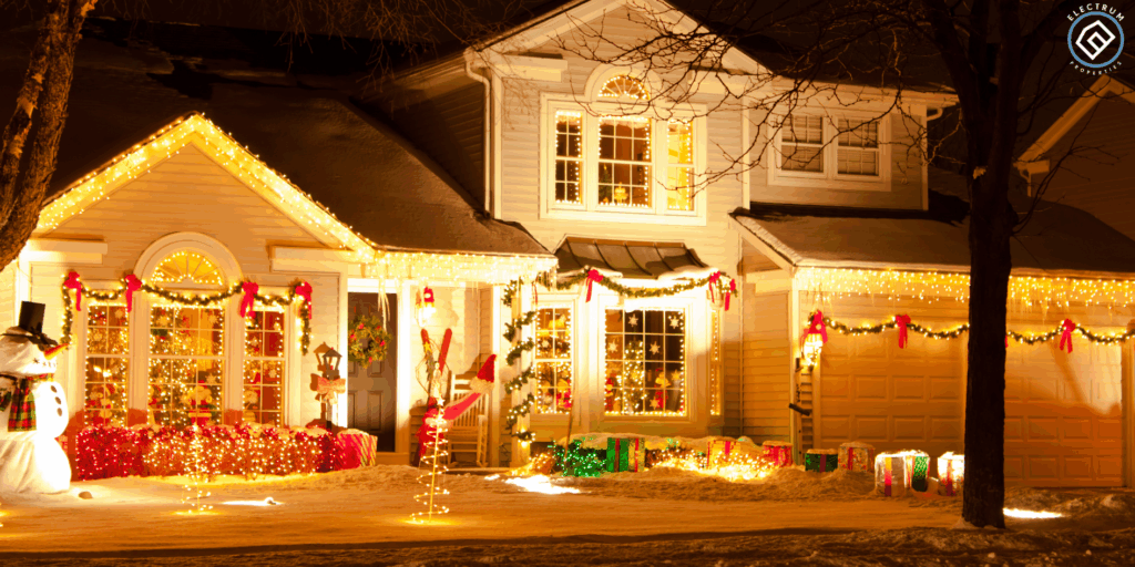 A warmly lit two-story home decorated with Christmas lights, garland, and holiday displays, illustrating the festive season—perfect for marketing messages about selling your house fast before or after the holidays. Snow covers the yard, and the Electrum Properties logo appears in the corner, emphasizing trusted local home-buying services.