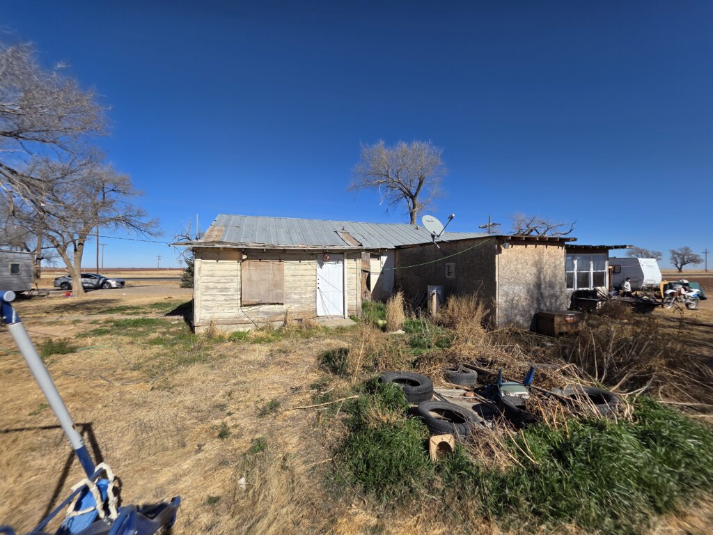 Distressed rural home with boarded windows and overgrown yard in West Texas, property purchased by Electrum Properties.