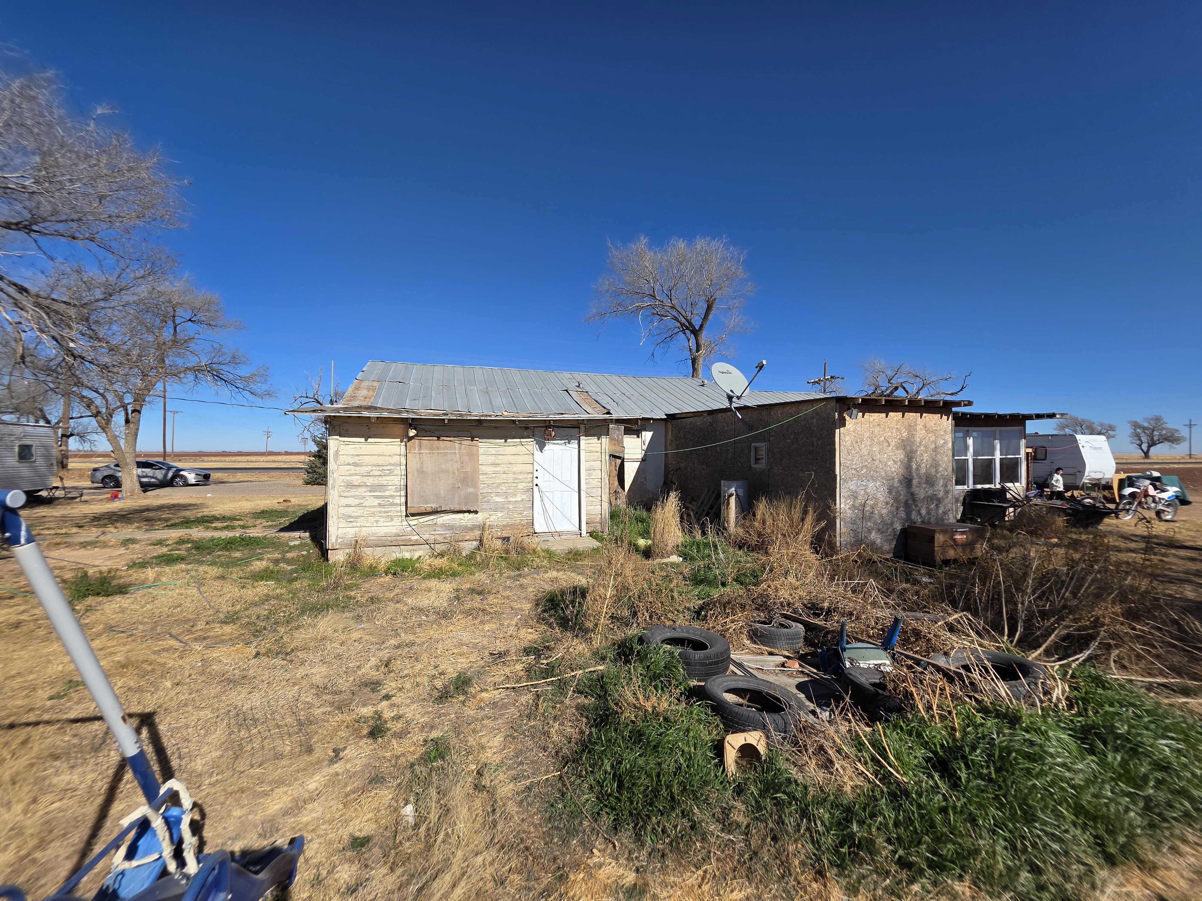Distressed rural home with boarded windows and overgrown yard in West Texas, property purchased by Electrum Properties.