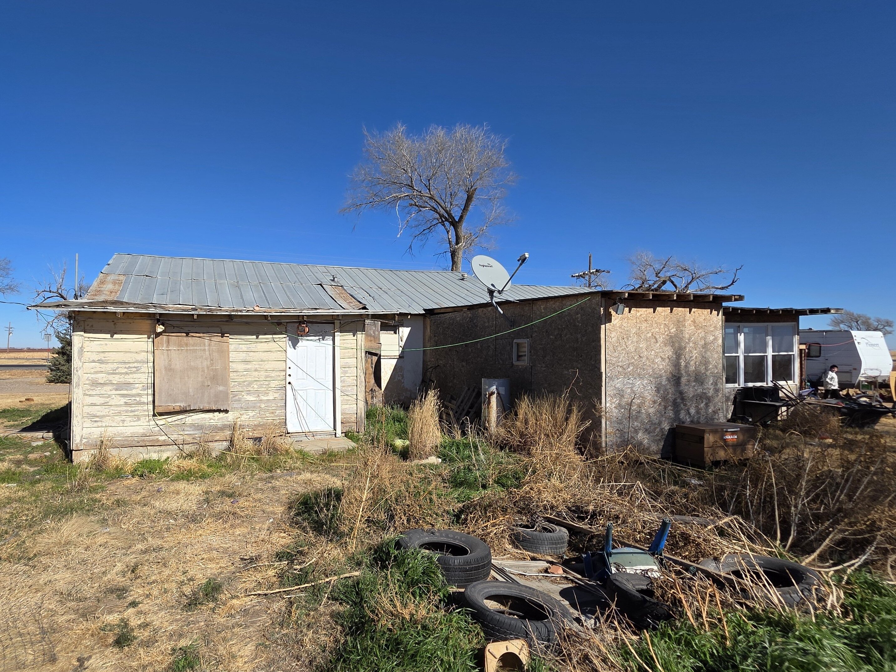 Distressed rural home with boarded windows and overgrown yard in West Texas, property purchased by Electrum Properties.