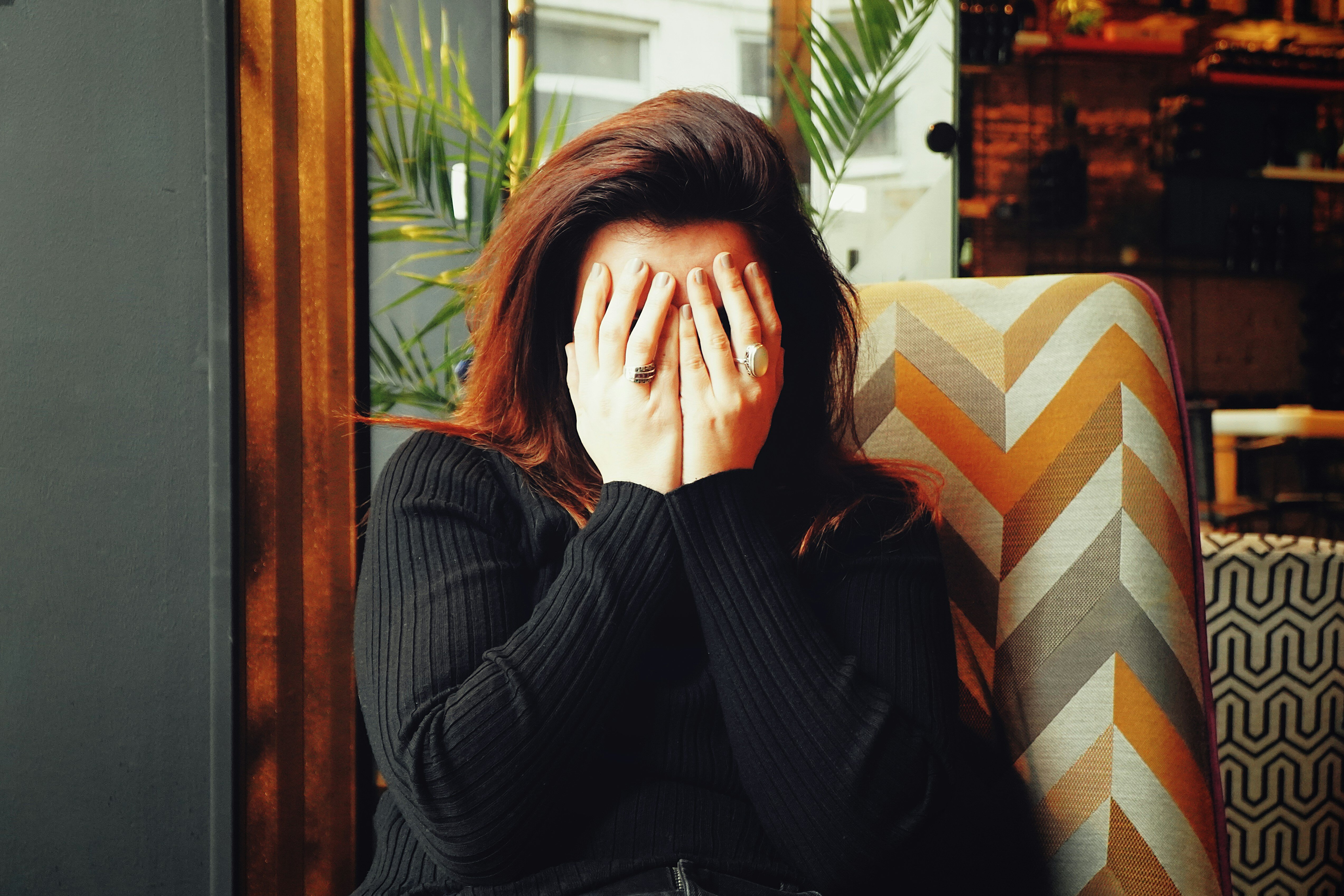 Image of a woman in a warmly-colored home, with her hands over her face, as in frustration