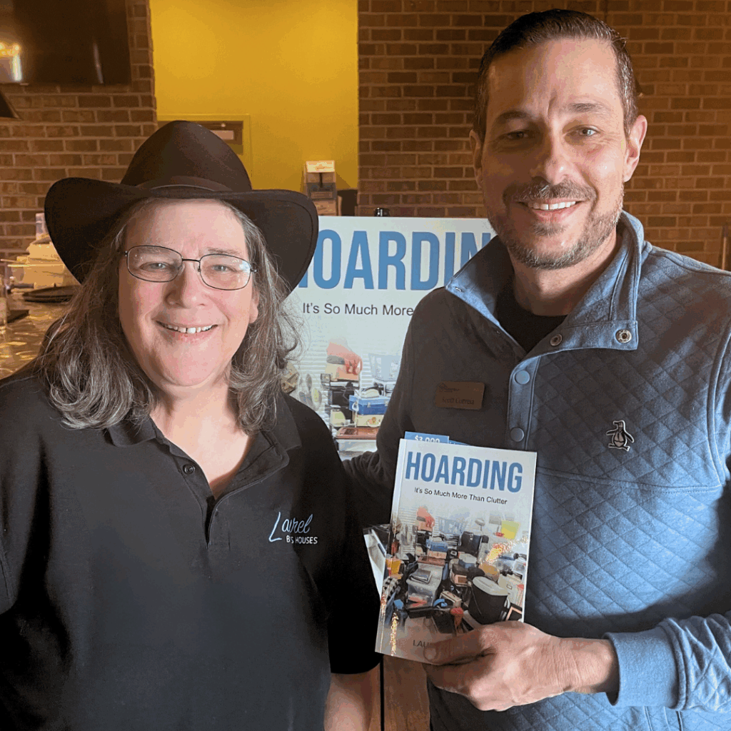 Laurel Sagen standing beside a young man at a book launch party for her book: Hoarding. The young man holds up a copy of the book with the cover facing the camera.