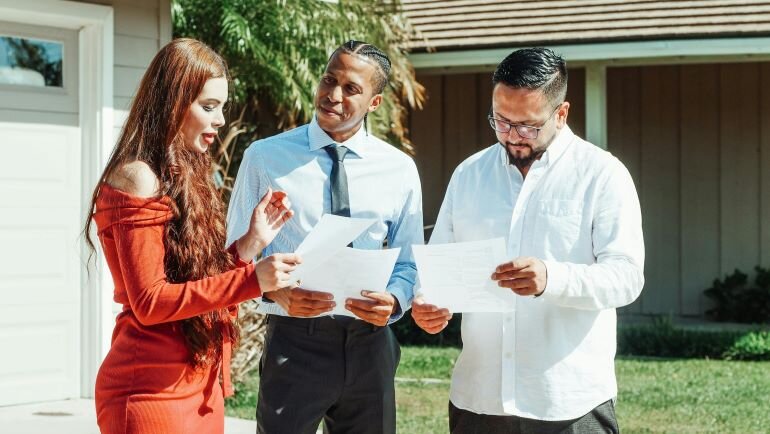 Three people standing outside a house and reviewing paperwork related to an inherited

property sale.